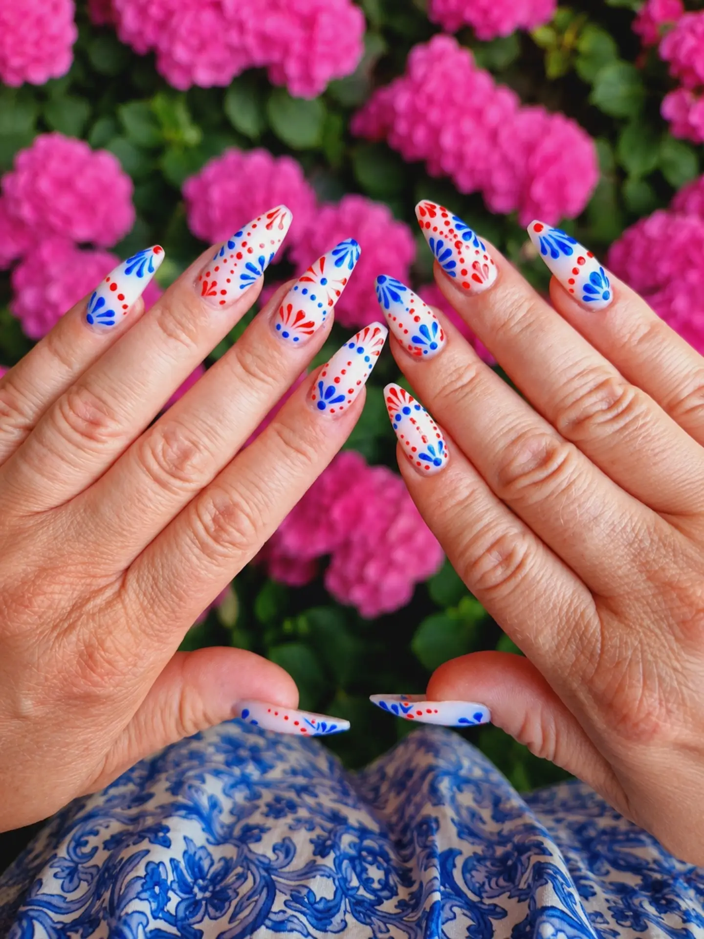 Hand-painted blue and red nail art photographed against pink flowers
